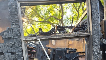 Charred wooden window frame revealing the burnt, collapsed interior of a home destroyed by fire.