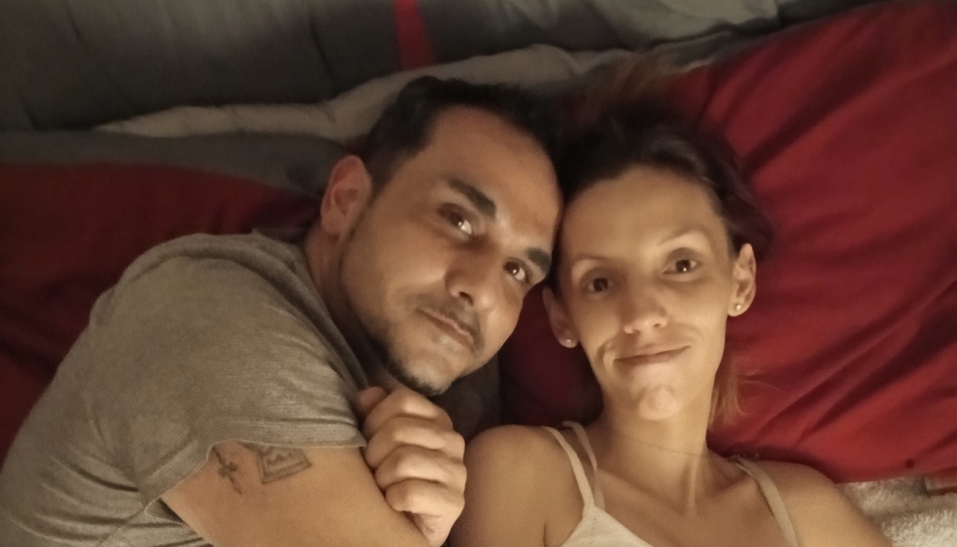 A man and a woman lie side-by-side on red pillows, smiling gently at the camera.