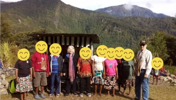 Community members and visitors standing together outside a small wooden shelter in a mountain valley.