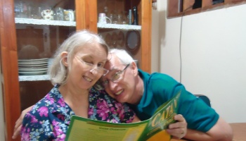 A smiling senior couple wearing glasses reading Catan board game instructions together.