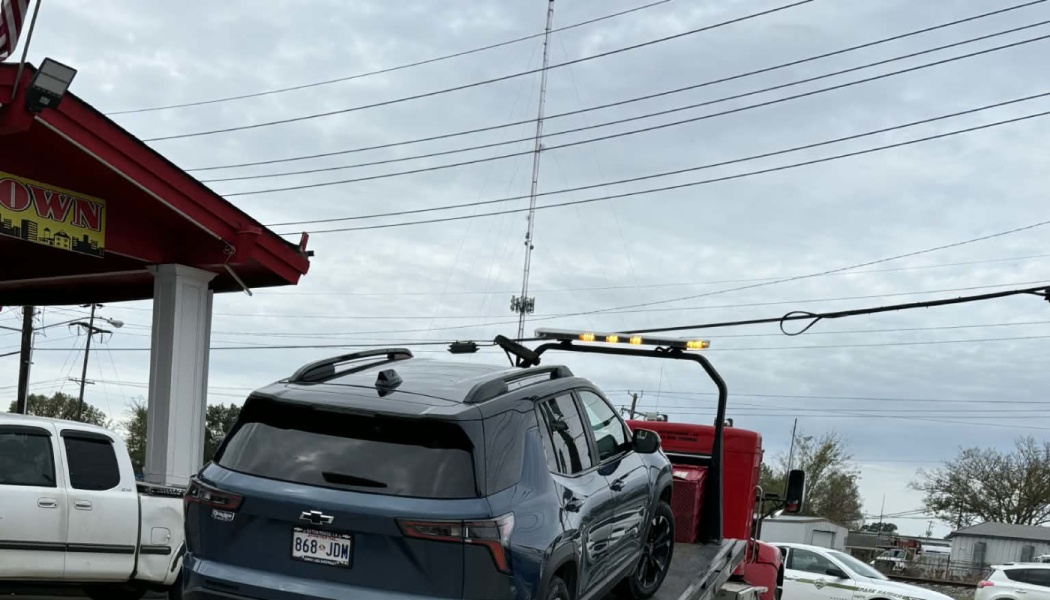 A dark blue Chevrolet SUV loaded onto a red flatbed tow truck with illuminated amber lights.