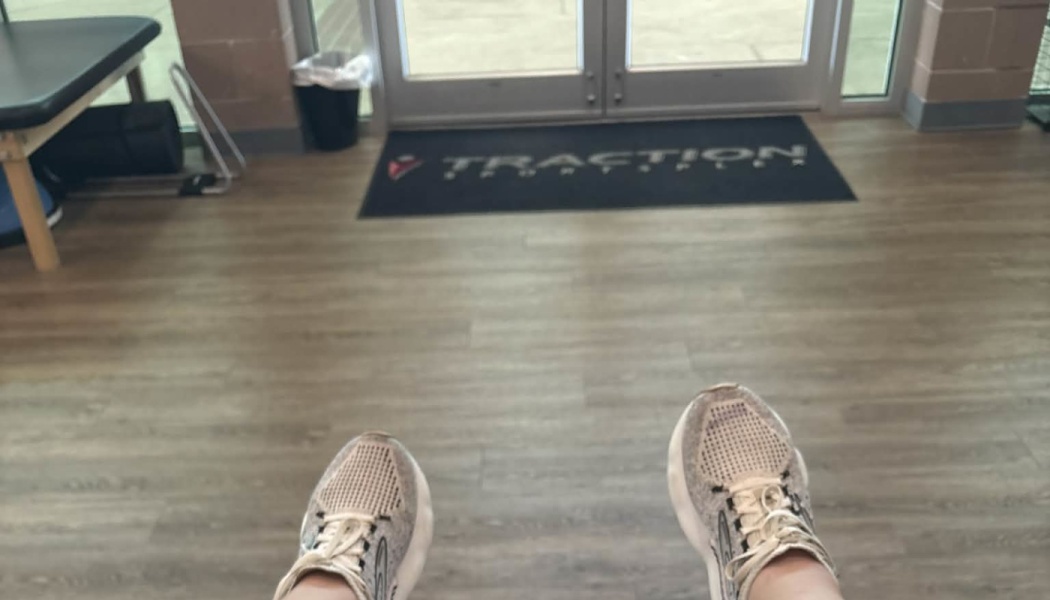 First-person view of feet in white running shoes facing the entrance doors of a sports facility.