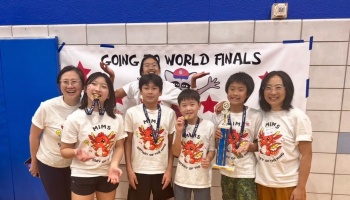 Smiling student team holding a trophy and wearing medals in front of a banner reading "Going to World Finals."