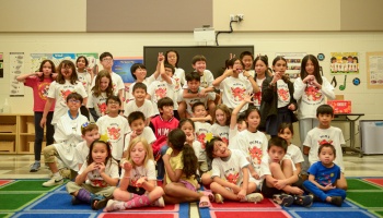 Diverse group of school children wearing matching dragon t-shirts making silly faces together in a classroom.