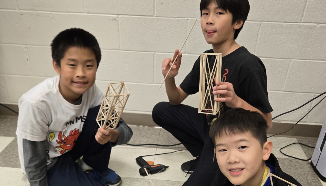 Three smiling boys hold balsa wood towers they built during a hands-on STEM engineering activity.