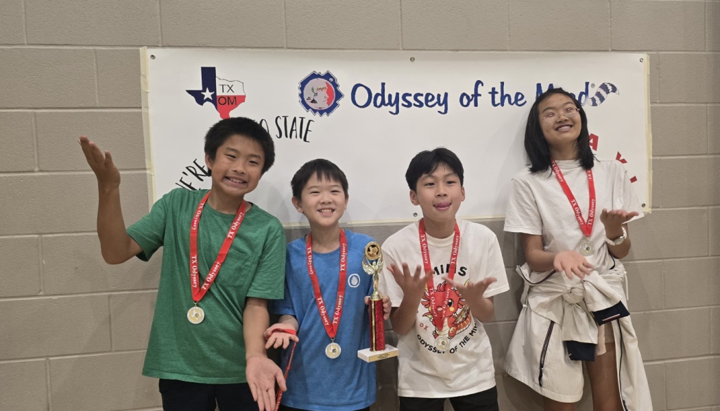 Four smiling students wearing medals pose with a trophy in front of an Odyssey of the Mind banner.