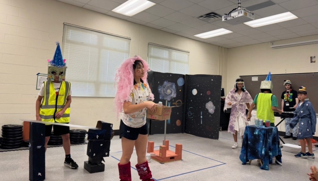 Students wearing creative homemade space costumes perform a skit in a classroom with space backdrops.