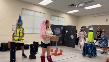 Students wearing creative homemade space costumes perform a skit in a classroom with space backdrops.