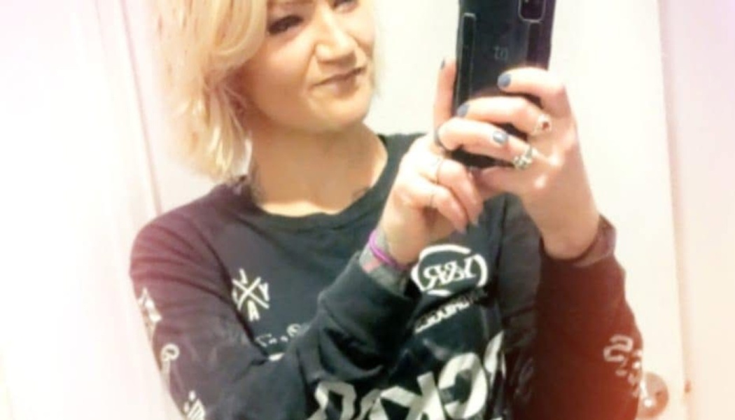 Woman with short blonde hair taking a mirror selfie in a black graphic long-sleeve shirt.