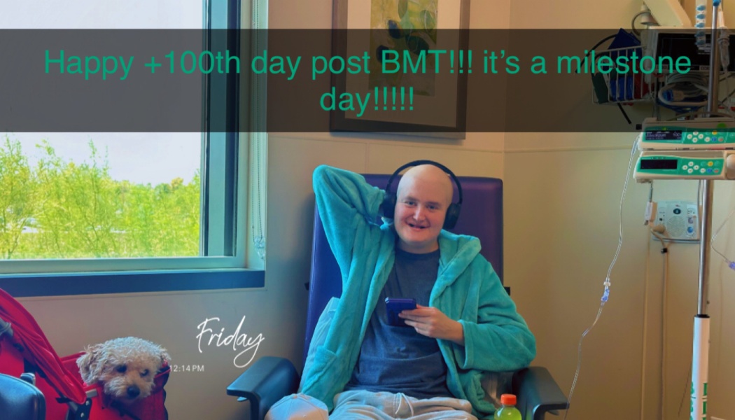 Smiling bald patient in a teal robe in a hospital chair next to a dog. Overlay text says: Happy +100th day post BMT!