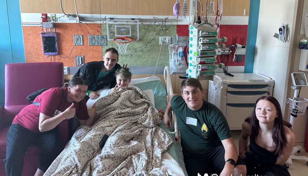 Family and friends smile and pose around a young patient lying in a decorated hospital bed.