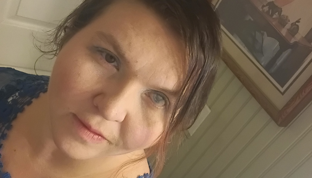 Close-up portrait of a woman with short dark hair wearing a blue lace top looking into the camera.
