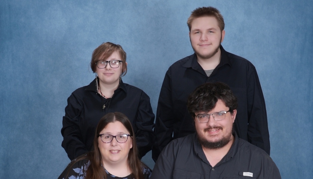 Four people smiling in a group portrait against a textured blue backdrop.