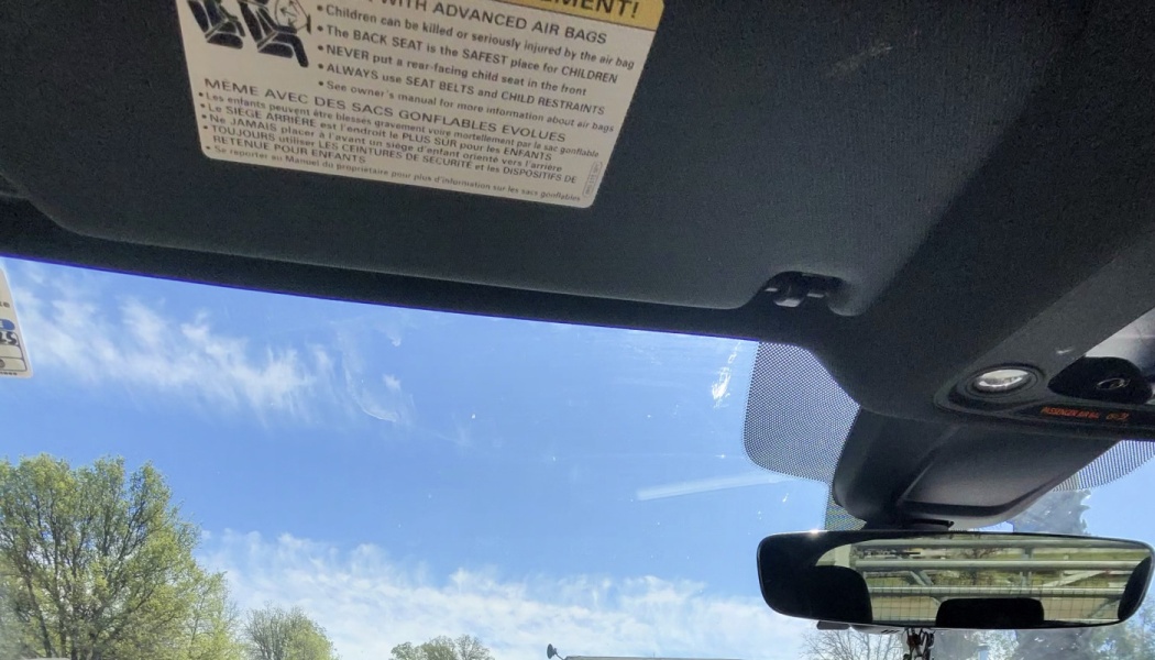 Interior view looking out a car windshield at a bright blue sky, showing the sun visor and rearview mirror.