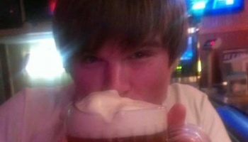 A young man taking a sip from a large mug of beer topped with thick white foam.