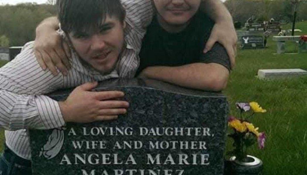 Two young men hugging a headstone inscribed "A loving daughter, wife and mother Angela Marie Martinez".