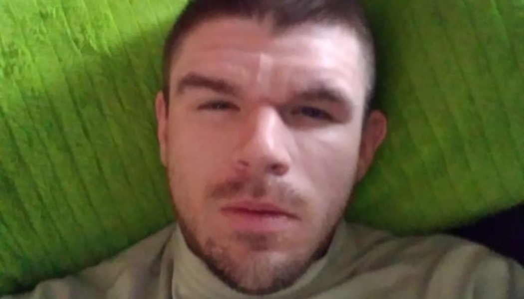 Close-up portrait of a man with short dark hair and facial hair lying against a bright green cushion.