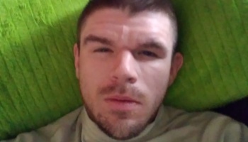 Close-up portrait of a man with short dark hair and facial hair lying against a bright green cushion.