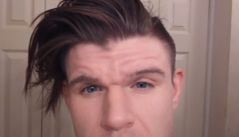 Close-up of a man with blue eyes and a dark brown, styled undercut haircut swept to one side.