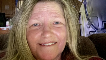 Close-up portrait of a middle-aged woman with long blonde hair and blue eyes, smiling at the camera.