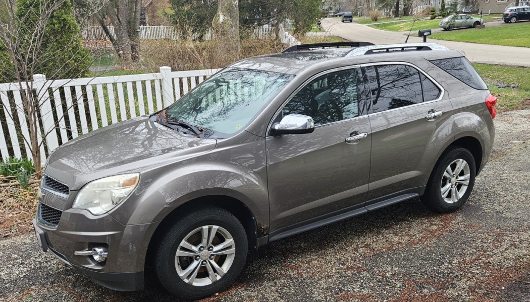 A metallic gray Chevrolet Equinox SUV parked on a gravel driveway in front of a white fence.