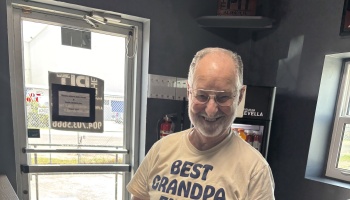 A smiling elderly man with glasses and a beard wearing a Best Grandpa t-shirt.