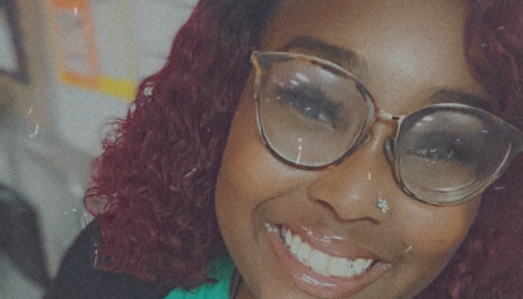 Close-up selfie of a smiling Black woman with curly red hair, stylish glasses, and a nose stud.