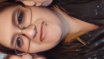 Close-up selfie of a smiling young woman with glasses and dark hair.