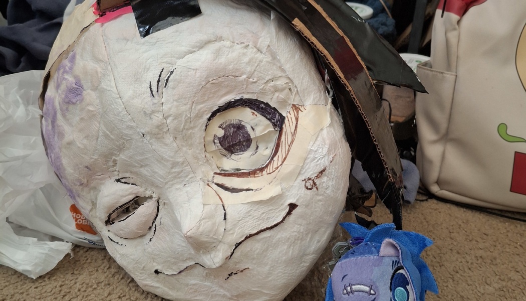 A paper-mache anime mask with hand-drawn eyes and expression, created as a work-in-progress cosplay project.
