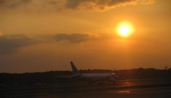 An airplane on a runway silhouetted against a bright, glowing golden sunset.