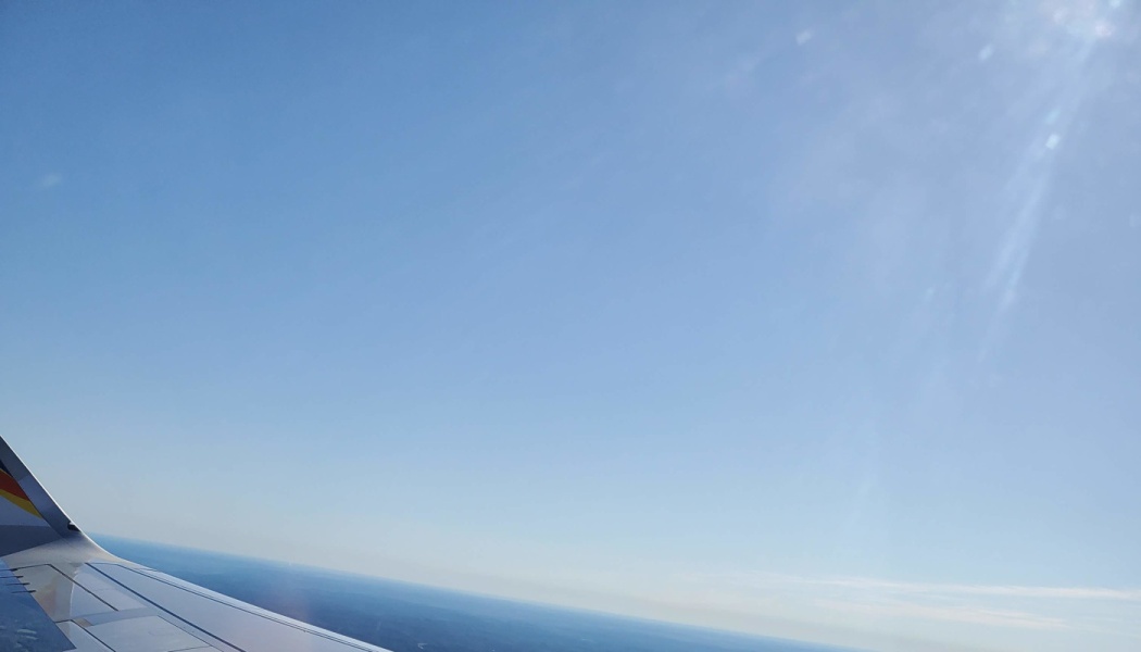 Airplane wing against a clear blue sky with bright sunlight shining from above.