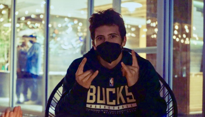 Young man wearing a face mask and Milwaukee Bucks hoodie, making rock-on hand gestures.
