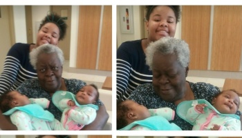 An elderly Black woman holds newborn twins while a smiling young woman stands behind her.