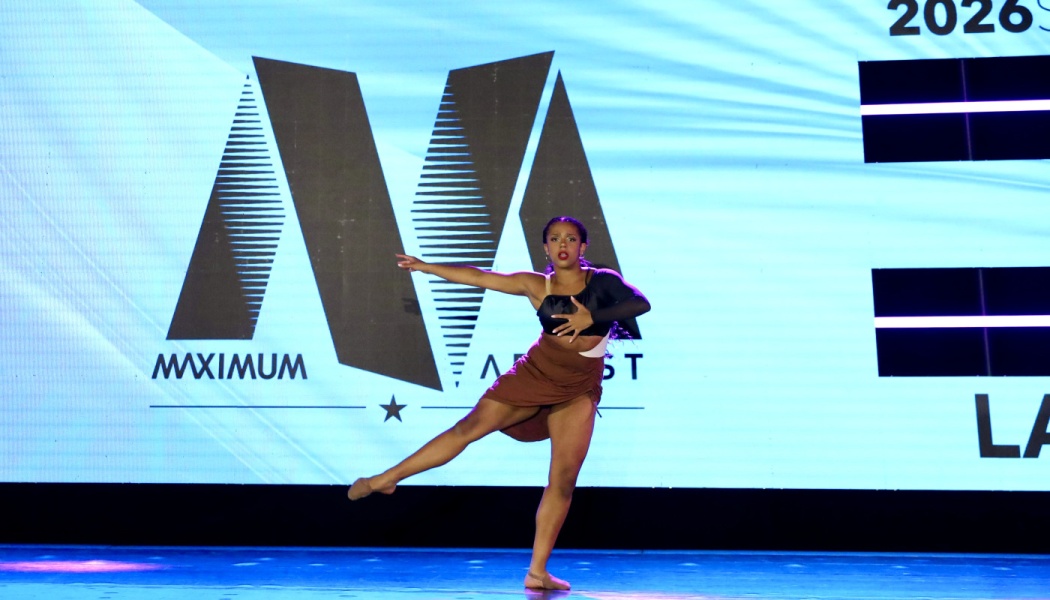 A female dancer striking an expressive pose on stage in front of a large blue backdrop screen.