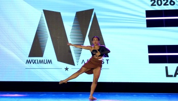 A female dancer striking an expressive pose on stage in front of a large blue backdrop screen.