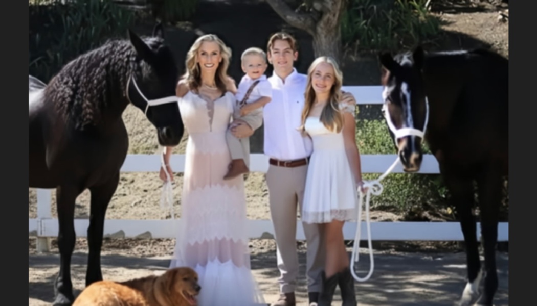 A smiling family dressed in white poses outdoors, flanked by two dark horses and a golden dog at their feet.