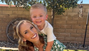 A smiling mother giving a piggyback ride to her young blonde son outdoors.