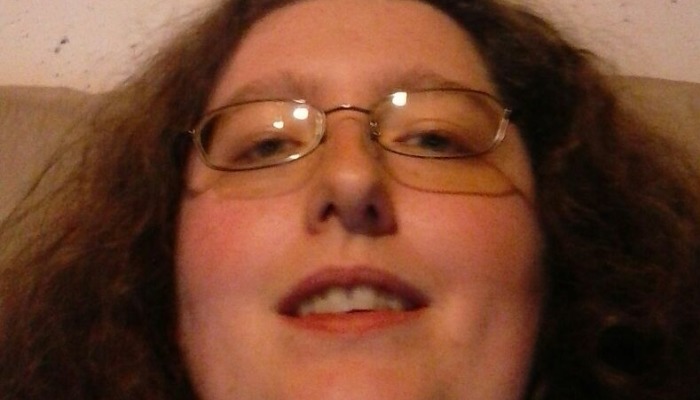 Close-up low-angle selfie of a person with long curly hair and glasses looking down at the camera.