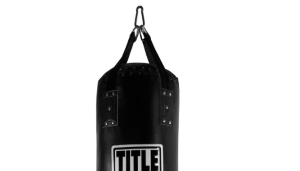 A black Title heavy punching bag hanging from straps against a white background.