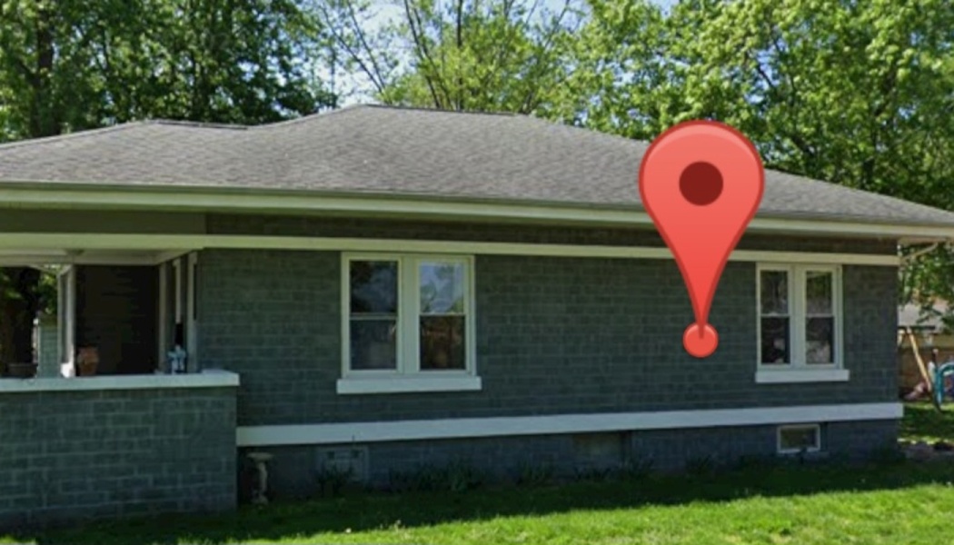 Single-story gray brick house with white-framed windows, a green lawn, and a red location pin marker.