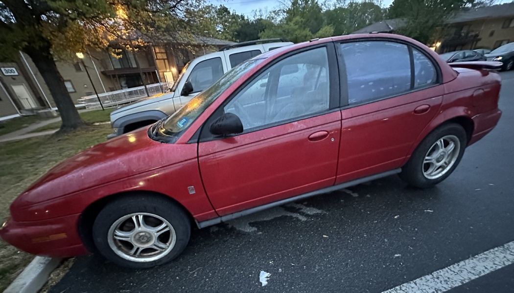 Side view of a red four-door Saturn sedan parked in an apartment parking lot.