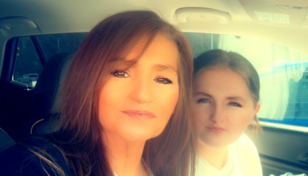 A woman with long brown hair and a young female taking a selfie together inside a car.