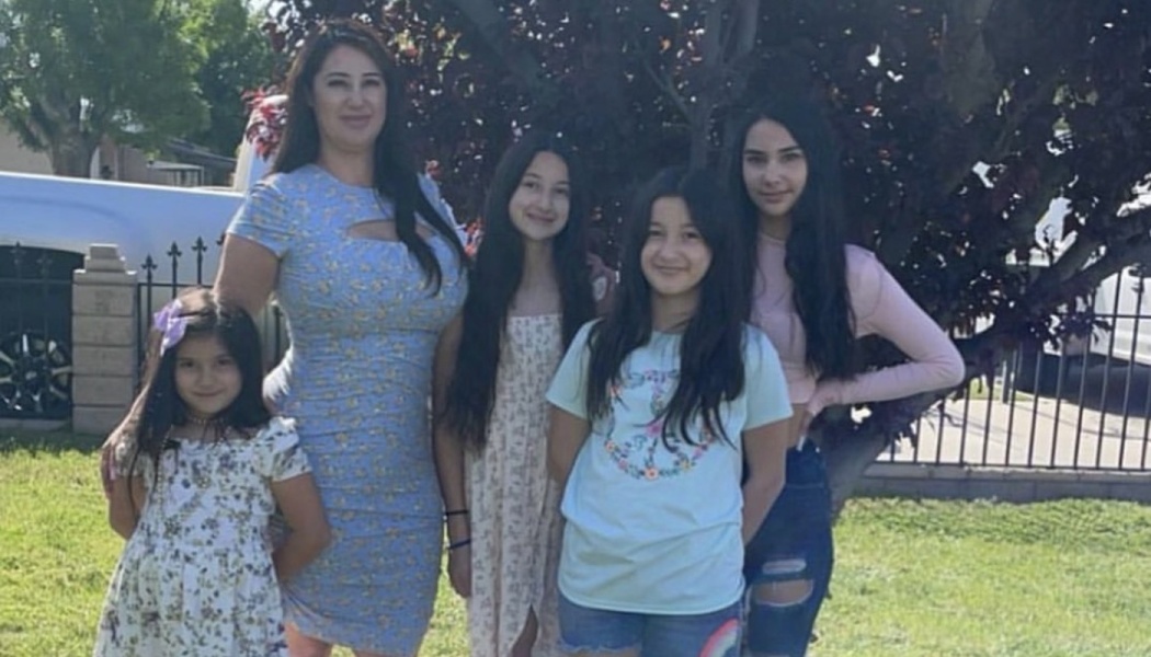 A mother and her four daughters smiling together outdoors on a grassy lawn.