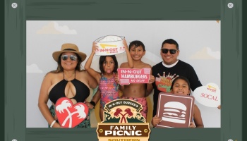 A smiling family of five poses with In-N-Out Burger signs and props at a family picnic photo booth.
