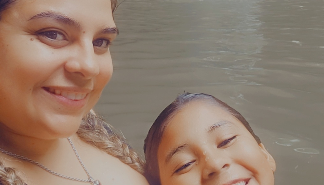 A smiling woman and a young child happily smiling together while swimming in open water.