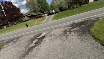 Deep water-filled potholes and cracked asphalt pavement along the edge of a residential street.
