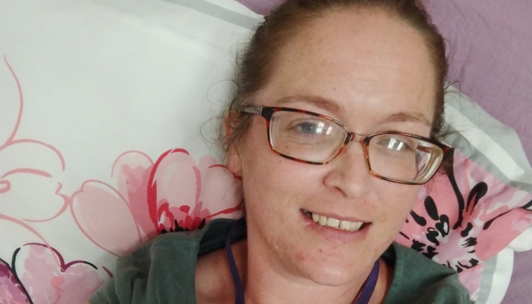 A woman wearing glasses smiles while resting on a floral pillow.