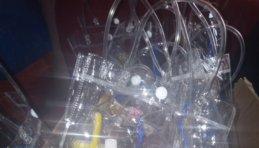 A pile of clear plastic tote bags with white snap closures and flexible tubing handles.