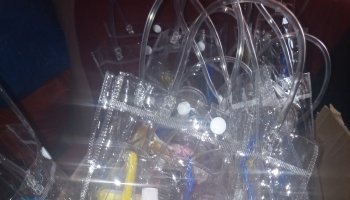 A pile of clear plastic tote bags with white snap closures and flexible tubing handles.