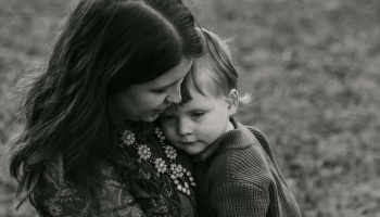 Black and white portrait of a mother tenderly embracing her young child, who rests his head on her chest.